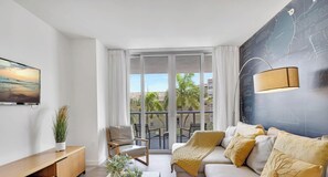 A modern living room with a sofa, a chair, a TV, and a large window. - Premium Floor · 2BR · Intracoastal · Beachwalk (Hallandale Beach)
