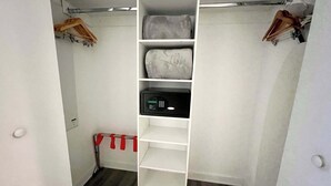 Un dressing avec des étagères et une tringle pour suspendre les vêtements, un objet rayé de rouge et de blanc posé sur le sol, et une porte blanche.