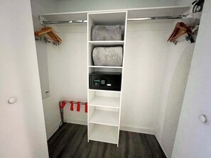 Ein begehbarer Kleiderschrank mit Regalen und Kleiderstangen, ein rot-weiß gestreifter Gegenstand auf dem Boden und eine weiße Tür.