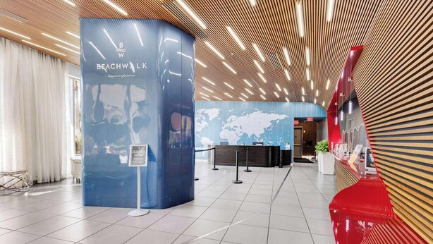 Eine moderne Lobby mit einer Rezeption, einer Weltkarte an der Wand und einem Schild, das darauf hinweist, dass Bade- oder Strandkleidung nicht erforderlich ist.