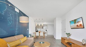 Ein modernes Wohnzimmer mit Sofa, Couchtisch und Essbereich, im Hintergrund eine Küche.