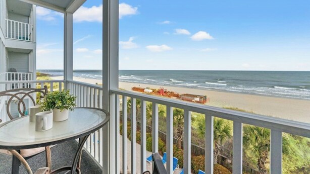 Ein Balkon mit Glastisch, Stühlen und Blick auf Strand und Meer.
