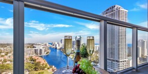 A balcony with a city view, two champagne flutes, and a bunch of grapes. - Top-Floor 1BR · Bay View · Beachwalk Resort & Gym (Hallandale Beach)