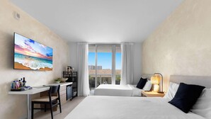 Ein Hotelzimmer mit Bett, Schreibtisch, Stuhl und einem großen Fenster mit Blick auf Gebäude.