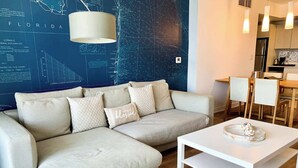 A modern living room with a sectional sofa, a white coffee table, and a map-themed wall. - South Intracoastal · Spacious 2BR Resort Condo (Hallandale Beach)