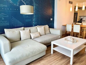 A modern living room with a sectional sofa, a white coffee table, and a map-themed wall. - South Intracoastal · Spacious 2BR Resort Condo (Hallandale Beach)