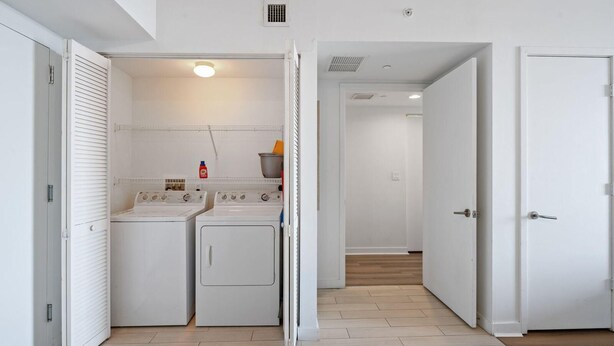 A laundry room with two washing machines and a dryer, a white door, and a hallway leading to another room. - Upper-Floor Bay View · 2BR Beachwalk Resort (Hallandale Beach)