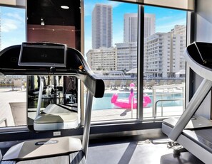 Ein Fitnessraum mit Trainingsgeräten und einem großen Fenster mit Blick auf die Stadt.