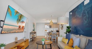 A living room with a large flat-screen TV, a dining area, a kitchen, and a large wall map. - Stylish High-Floor 2BR · Beachwalk Resort (Hallandale Beach)