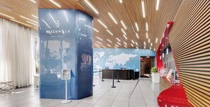 A modern hotel lobby with a curved reception desk, a world map on the wall, and a wooden ceiling design. - Stylish High-Floor 2BR · Beachwalk Resort (Hallandale Beach)
