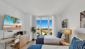 A hotel room with a bed, desk, and a large window with a city view. - Stylish High-Floor 2BR · Beachwalk Resort (Hallandale Beach)
