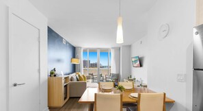 A modern kitchen with a built-in oven, a dining area with a wooden table and chairs, and a large window with a city view. - Spacious 1BR - Intracoastal View (Hallandale Beach)
