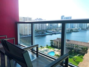 Ein Balkon mit Blick auf einen Fluss und eine Stadtansicht, ein Schwimmbecken und eine rote Wand.