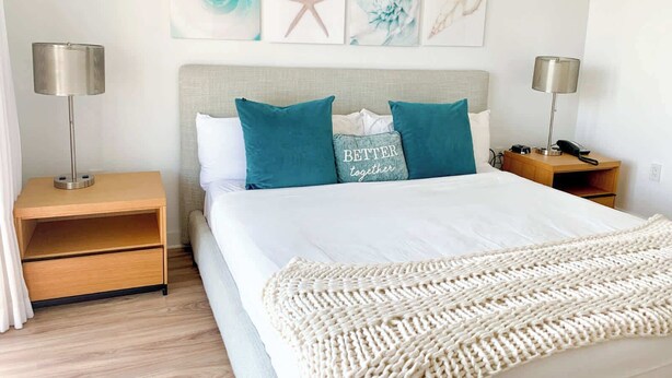 Habitación de hotel ordenada con una cama, dos mesitas de noche, una lámpara y decoración en la pared.