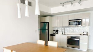 Una cocina moderna con armarios blancos, electrodomésticos de acero inoxidable y una mesa de comedor de madera con sillas.