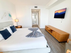 A hotel room with a bed, a TV mounted on the wall, and a wooden bench. - Sunset View Apt | Pool, Gym & Beach Shuttle (Hallandale Beach)