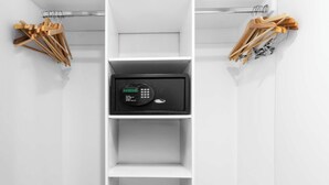 Ein weißer Kleiderschrank mit einem schwarzen elektronischen Gerät in der Mitte, hölzernen Kleiderbügeln oben und unten sowie einem Metallgestell mit Bügeln auf der rechten Seite.