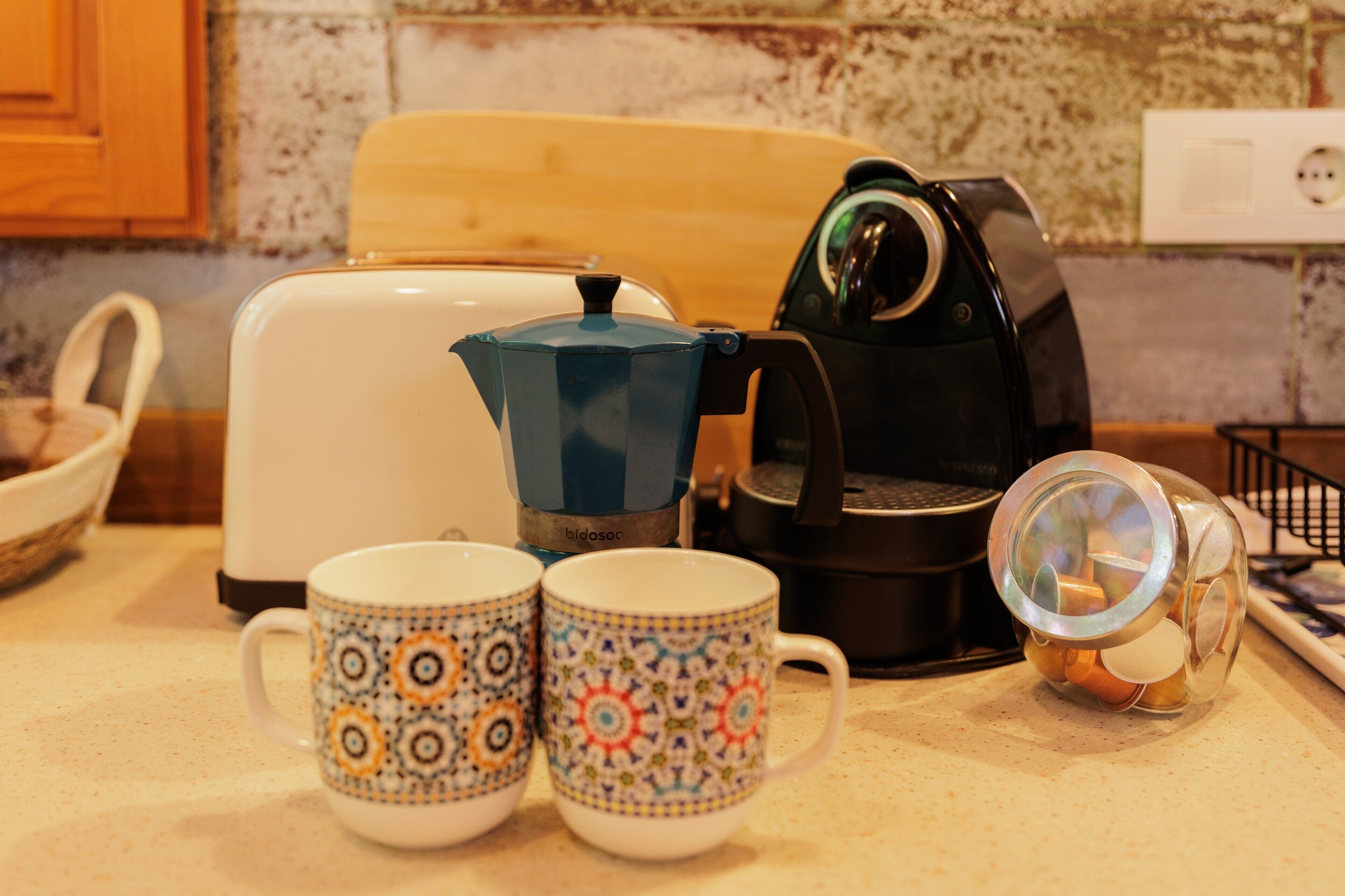 Une cuisine équipée d’une machine à café, d’un grille-pain et de deux tasses à motifs posées sur le comptoir.