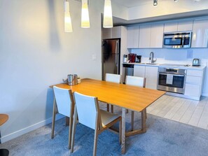 A modern kitchen with stainless steel appliances, a wooden dining table, and white chairs. - Breathtaking Bay View · 2BR · Beachwalk (Hallandale Beach)