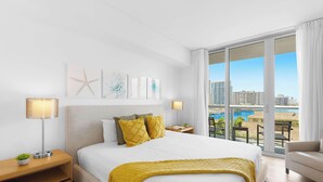 Une chambre d’hôtel avec un grand lit, une vue sur la ville et un balcon aménagé avec du mobilier d’extérieur.