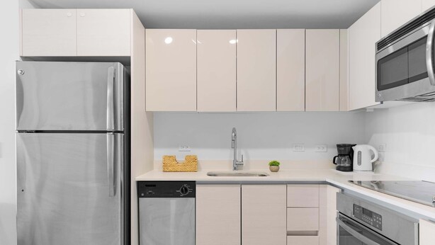 Une cuisine moderne dotée d’appareils électroménagers en acier inoxydable, de meubles de couleur claire et d’un lave-vaisselle encastré.