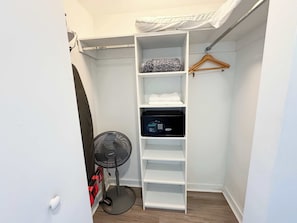 A walk-in closet with a white shelving unit, a black appliance, and a standing fan. - Sunset View Condo · 2BR Beachwalk Resort (Hallandale Beach)