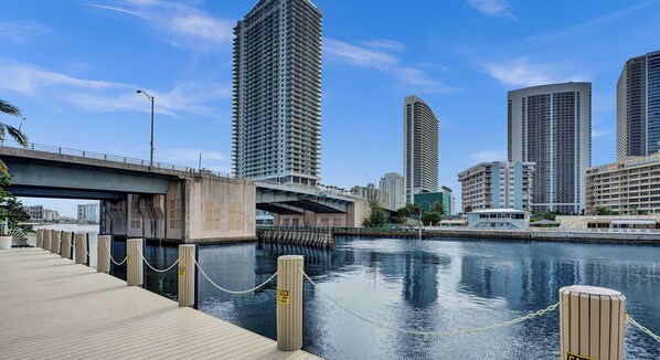 A waterfront cityscape with high-rise buildings, a bridge, and a dock with caution signs. - Bright 1BR  Waterway View & Resort Lifestyle (Hallandale Beach)
