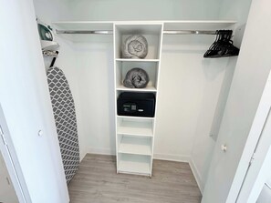 A walk-in closet with a white shelving unit, a black electronic device, and a patterned shower curtain. - Bright Studio | Intracoastal View | Pininfarina (Hallandale Beach)