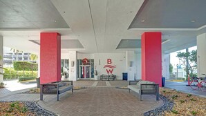 A spacious lobby with a modern design, featuring a prominent logo on the wall, a seating area with benches, and a view of the building's entrance. - Upper-Floor Studio | Resort Pool & Beach (Hallandale Beach)