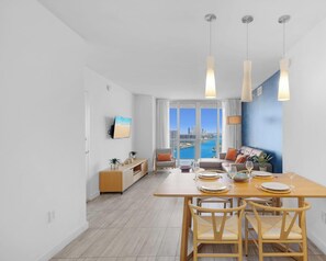A modern dining area with a wooden table, chairs, and hanging pendant lights. - Spacious 1BR · Sunset View · Beachwalk Resort (Hallandale Beach)