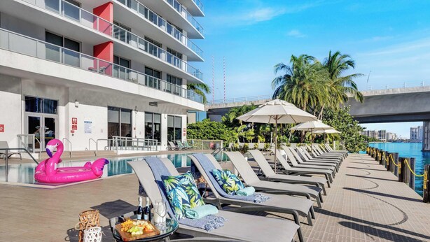 A poolside area with lounge chairs, umbrellas, and a flamingo float. - Spacious 1BR · Sunset View · Beachwalk Resort (Hallandale Beach)