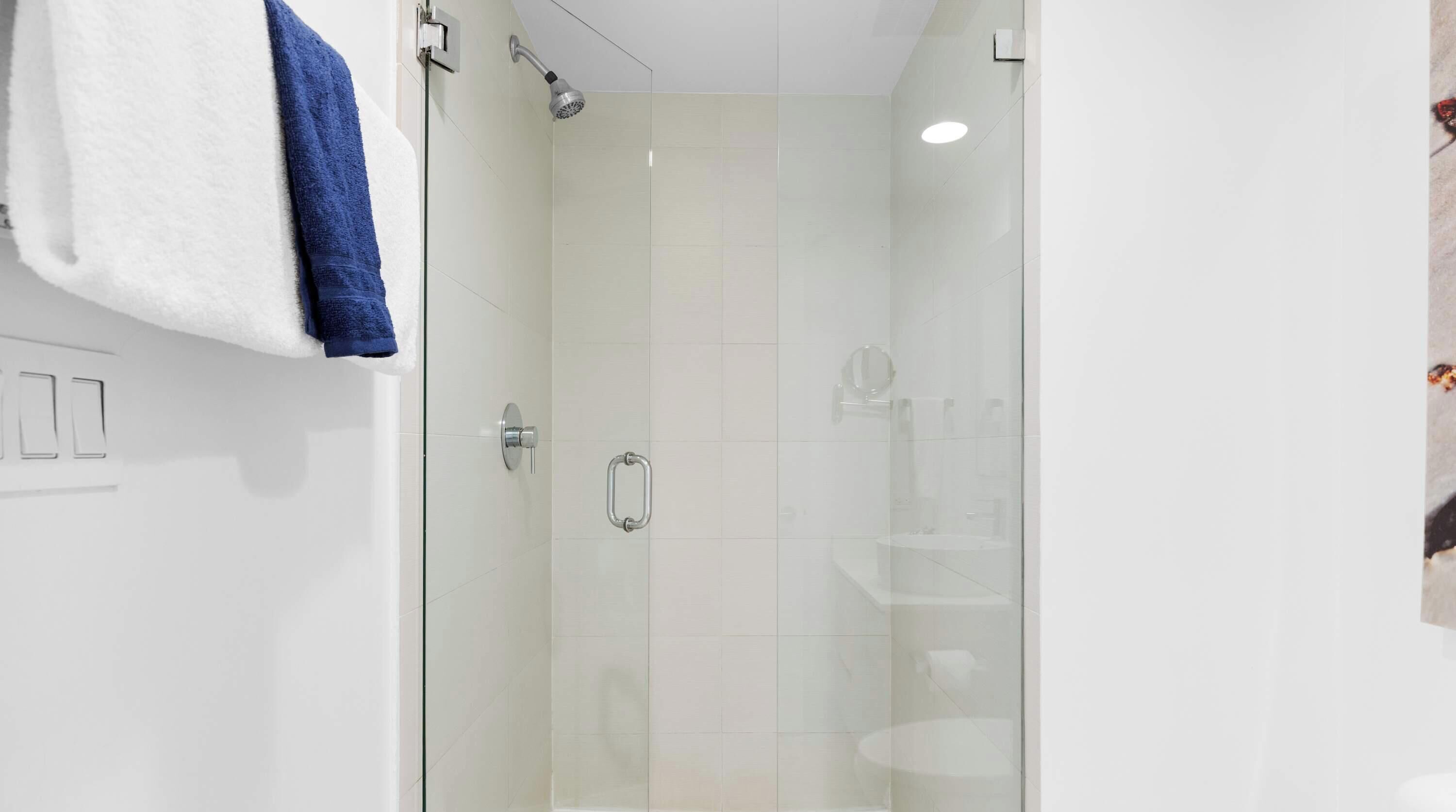 Ein modernes Badezimmer mit einer Duschkabine aus Glas, einer weißen Wand und einem Handtuchhalter mit einem blauen Handtuch.