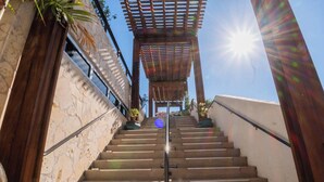 Eine Treppe führt zu einem überdachten Bereich mit einer Pergola, umgeben von Steinmauern und Topfpflanzen.
