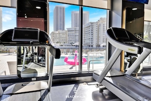 A gym with treadmills and a view of a cityscape through large windows. - Breezy Studio w/ Marina View & Balcony (Hallandale Beach)