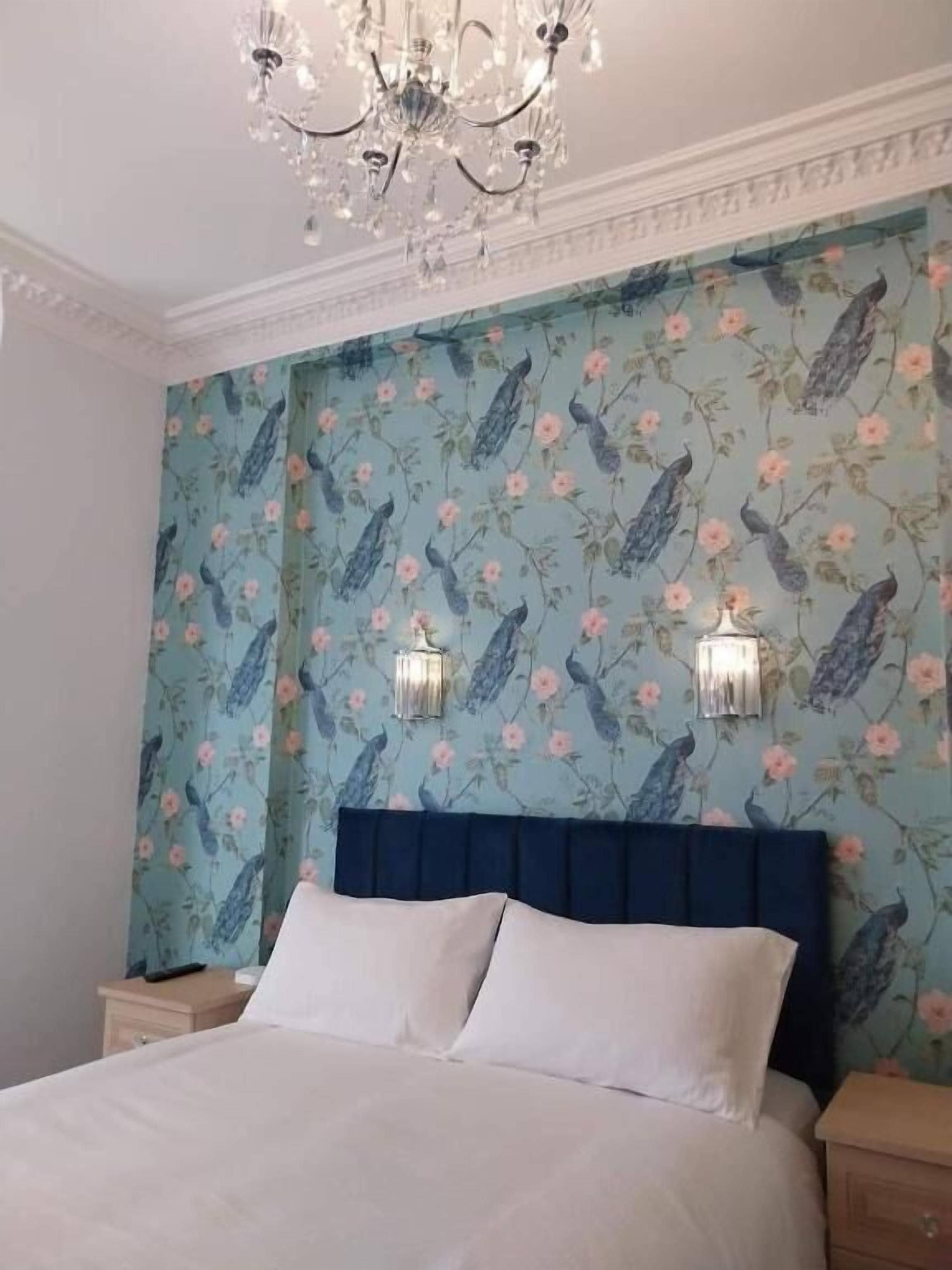 Un dormitorio con cama, candelabro y papel tapiz floral.