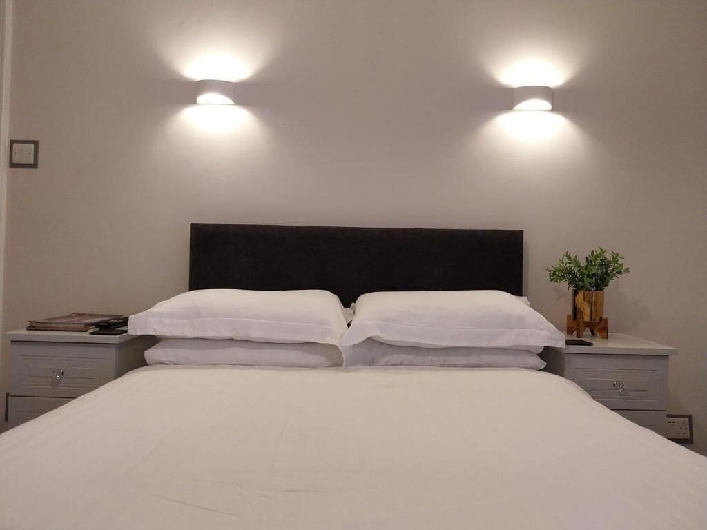 A neatly made bed with white linens, two bedside tables with lamps, and a small potted plant on one table.