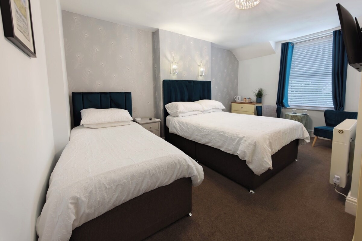 A hotel room with two beds, a desk, a chair, a TV, and a window with blinds.