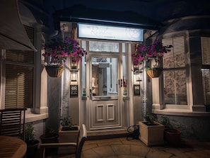 Entrada de hotel con un letrero que dice 'The Rosedene at Number 10', plantas en macetas, una puerta y un pequeño área de estar al aire libre.