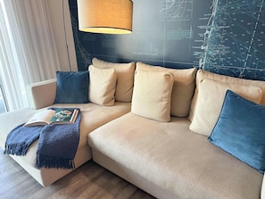 Ein beiges Sofa mit blauen Kissen und einer blauen Decke, eine Lampe und eine Karte an der Wand.