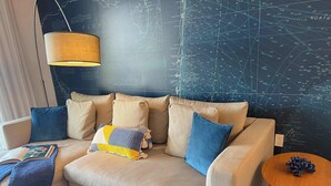 A modern living room with a sectional sofa, a small round table, and a map-themed wall. - 1BR with Stunning Intracoastal View, Private Balcony & Full Kitchen (Hallandale Beach)