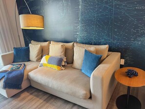 A modern living room with a sectional sofa, a small round table, and a map-themed wall. - 1BR with Stunning Intracoastal View, Private Balcony & Full Kitchen (Hallandale Beach)