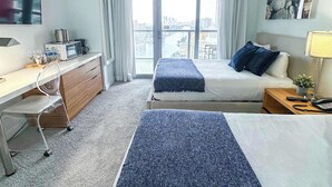 A hotel room with a bed, a desk, a chair, a TV, and a window with a city view. - Beachwalk Studio | Bay & Skyline Vistas (Hallandale Beach)