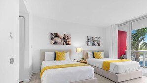 Ein Hotelzimmer mit zwei Betten, einem Balkon mit roter Akzentwand und Bildern an den Wänden.