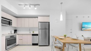 Eine moderne Küche mit Edelstahlgeräten, ein Essbereich mit einem Holztisch und einem an der Wand befestigten Fernseher.