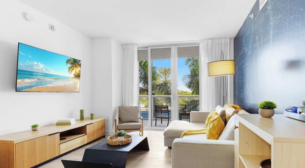 A modern living room with a large TV, a sofa, a chair, and a dining area. - Intracoastal Gem · 2BR · Pool & Resort (Hallandale Beach)