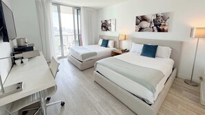 Ein Hotelzimmer mit zwei Betten, einem Schreibtisch, einem Stuhl, einem Fernseher und Bildern an den Wänden.