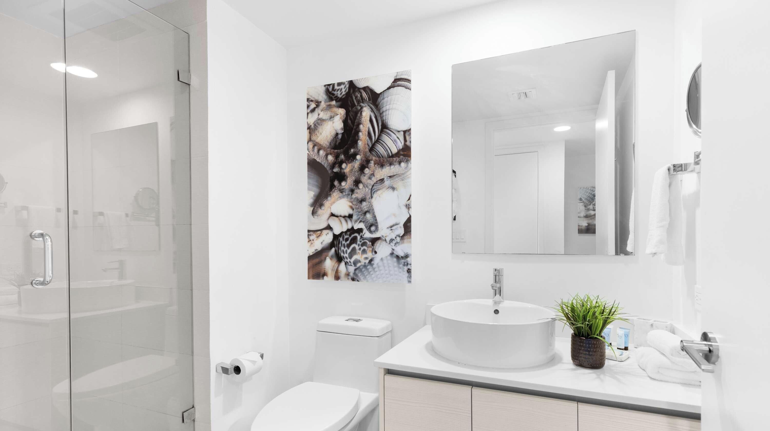 A modern bathroom with a glass shower enclosure, a toilet, a sink with a mirror, and a decorative wall piece.