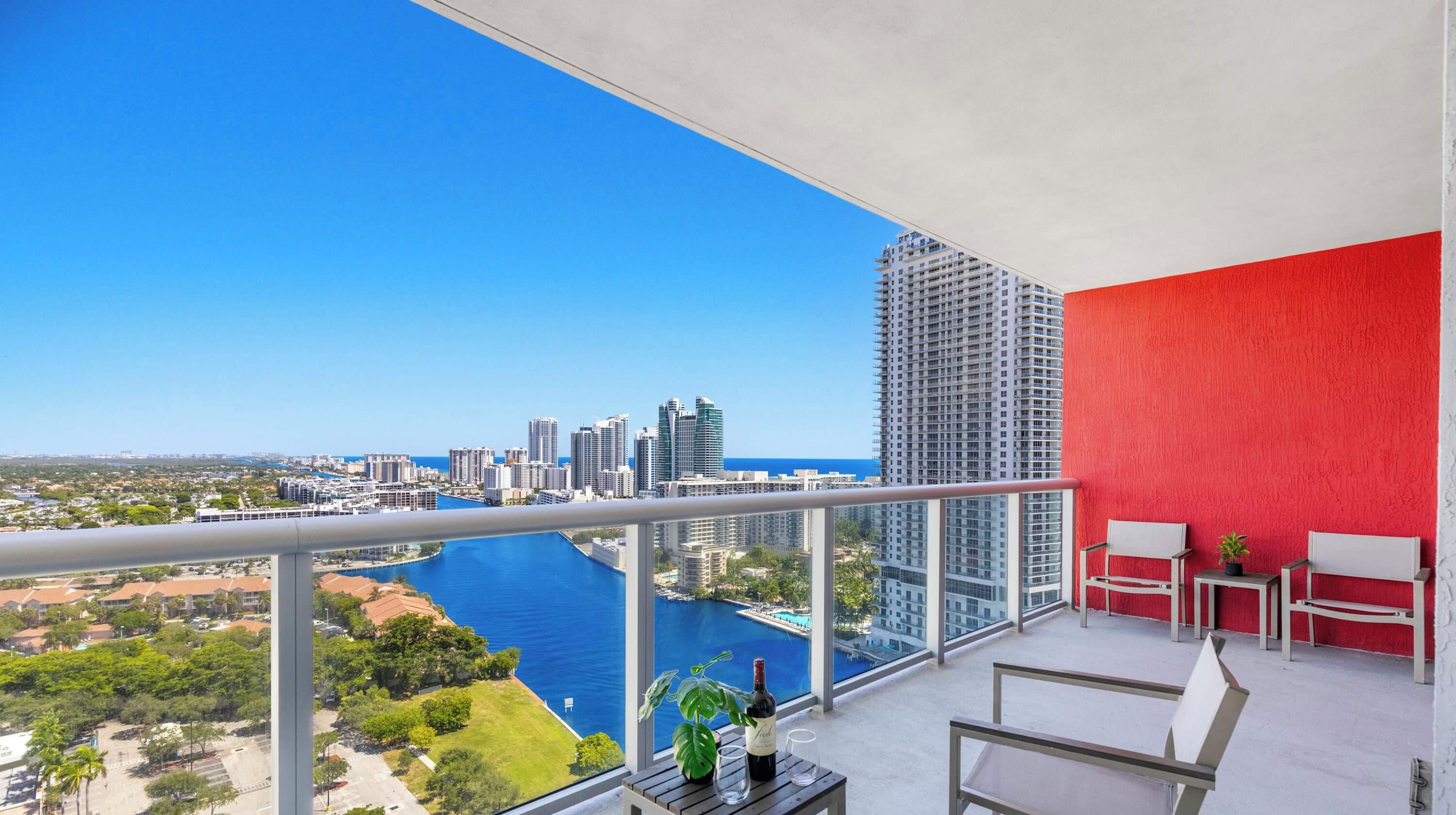 A balcony with a city view, a red wall, and a table with a bottle and glass.