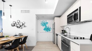 A modern kitchen with a microwave, oven, and sink. There is a dining area with a table and chairs. - Resort Living 2BR · Bay View Hallandale (Hallandale Beach)