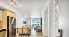 A modern kitchen with a stainless steel refrigerator, dining table with chairs, and a TV mounted on the wall. - Top-Floor Bay View · 2BR Beachwalk Resort (Hallandale Beach)